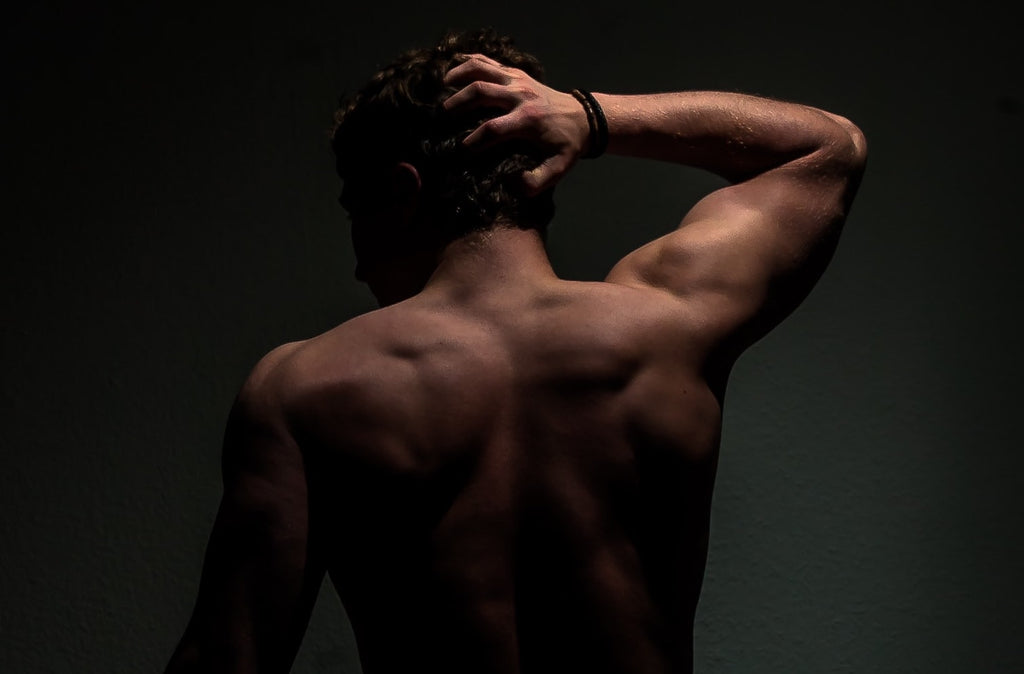 shirtless guy from behind with one arm touching his head. Dark background moody images