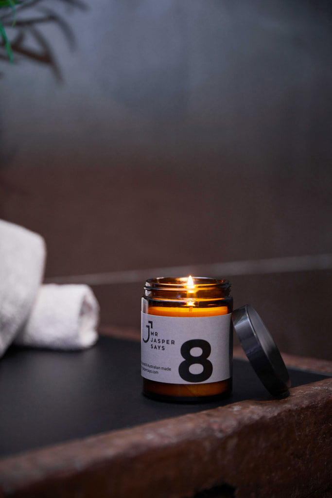 A lit medium candle number 8 with the lid leaning against the right side, placed on a rustic sink and dark and moody colour scheme